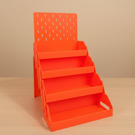 An orange plastic multi-tier desk organizer with a pegboard back panel, shown on a wooden desk with a laptop and other office items in the background.
